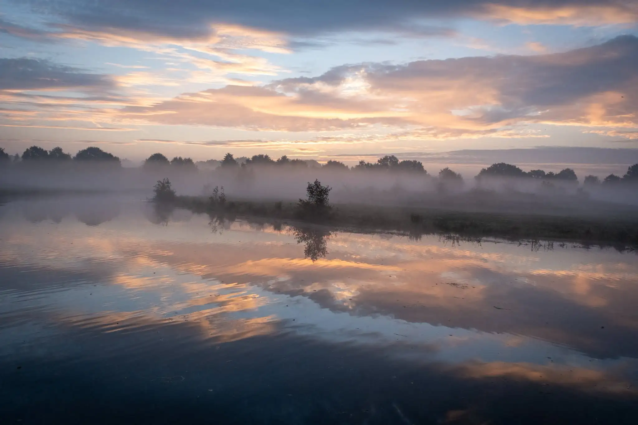 Zonsopkomst boven het water met mist en weerspiegelende wolken